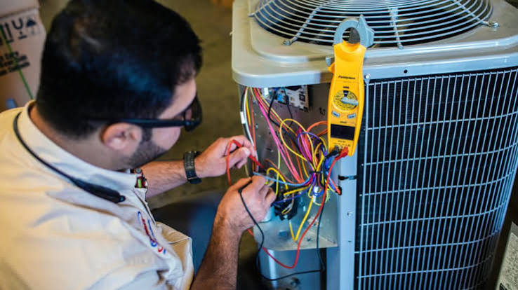 Technician testing electrical connections on an outdoor HVAC unit
